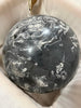 A polished round stone ornament or decorative ball with a dark gray and white marbled pattern, resting on a soft beige fabric background.