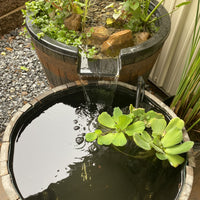 Small pond inside whiskey barrel with water feature and plants in a garden setting