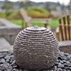 Decorative stone sphere in a garden setting with flowers and rocks.