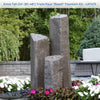 Three tall faux basalt stone fountain spires arranged in a cluster, shown outdoors in a garden setting with flowers, a stone wall, and patio furniture. A text banner at the top reads 'Extra Tall (24'-36'-48") Triple Faux "Basalt" Fountain Kit - LA7475'.