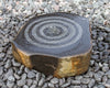 A natural stone fountain with concentric circular ripples on top, set on a bed of small gray pebbles.