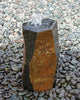 A natural stone fountain with a small waterfall spouting from the top, set in a bed of smooth river stones. The stone features a dual-tone design with a dark charcoal gray outer face and a warm, textured rust-orange and brown inner face.