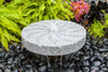Stone water fountain surrounded by greenery and pebbles