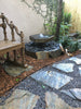 Small water fountain in a garden setting with a wooden bench and stone pathway. Black pebbles as an option.