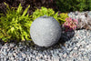 Decorative stone sphere in a garden setting with flowers and rocks.