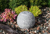 Decorative stone sphere in a garden setting with flowers and rocks.