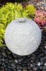 Decorative stone sphere in a garden setting with flowers and rocks.