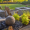 Decorative stone sphere in a garden setting with flowers and rocks.