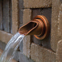 Atlantic Water Gardens Copper Finish Olivett Wall Spout set within patio hardscape
